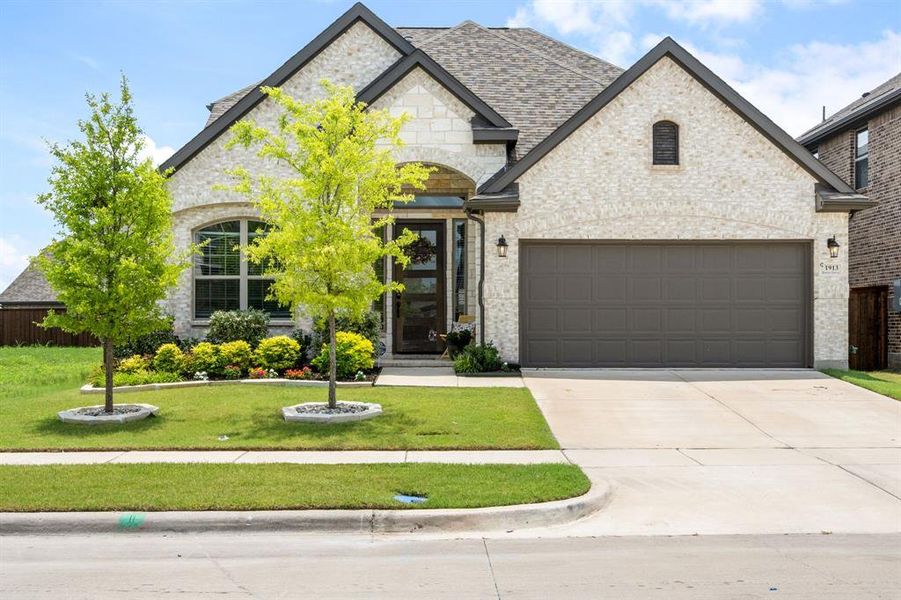 Brick and stone facade residence featuring an arched entry, a two-car garage, and mature landscaping Brick and stone facade residence featuring an arched entry, a two-car garage, and mature landscaping