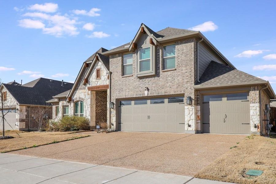 View of front of property with stone siding, concrete driveway, a garage, brick siding, and a shingled roof