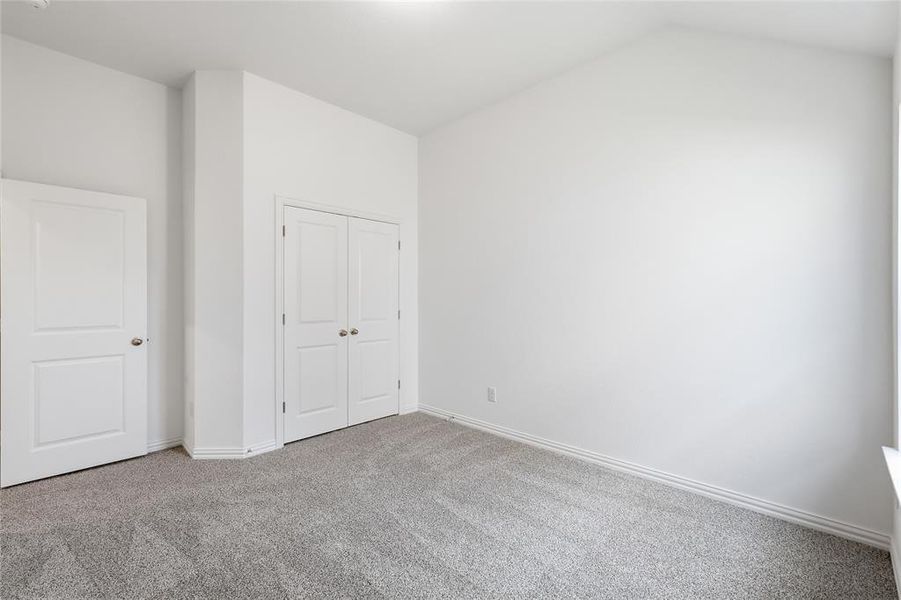 Spacious room featuring vaulted ceilings, neutral-toned walls, plush grey carpeting, and white trim