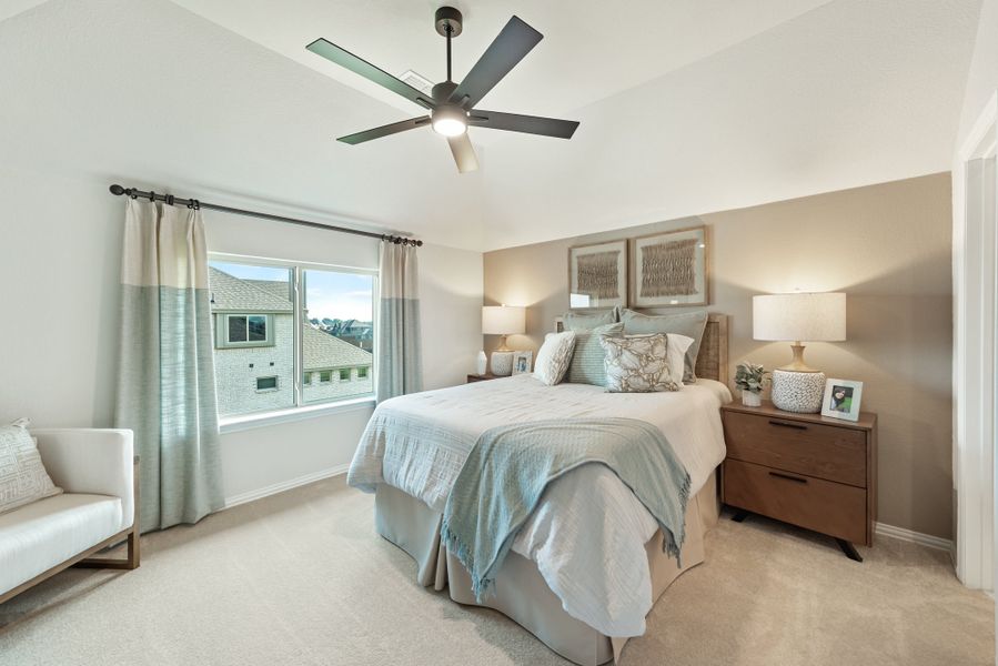 Bedroom with vaulted ceiling, ceiling fan, carpet flooring, and large window with neutral curtains