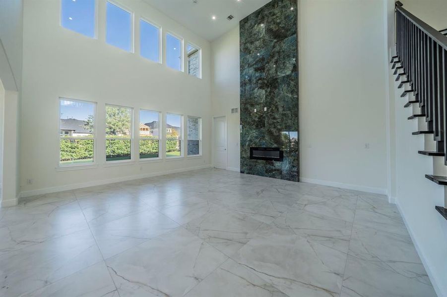 Unfurnished living room featuring light marble finish floors, a high end fireplace, a towering ceiling, and stairway Unfurnished living room featuring light marble finish floors, a high end fireplace, a towering ceiling, and stairway