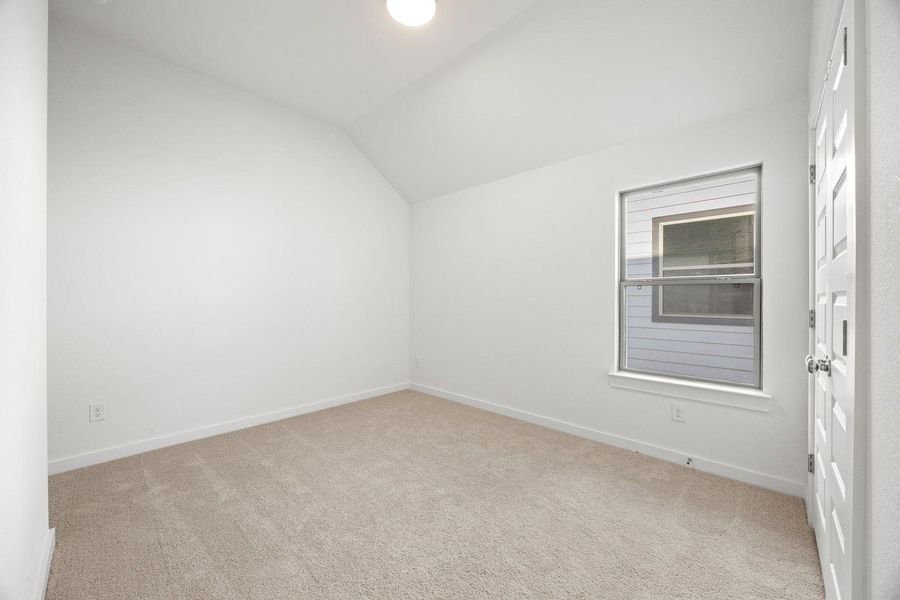 A spacious room offers comfortable carpeting, sloped ceilings, and natural illumination from an exterior window.