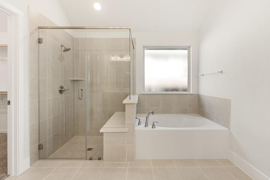 Bathroom with glass-enclosed tile shower and soaking tub with chrome fixtures on beige tile floors Bathroom with glass-enclosed tile shower and soaking tub with chrome fixtures on beige tile floors