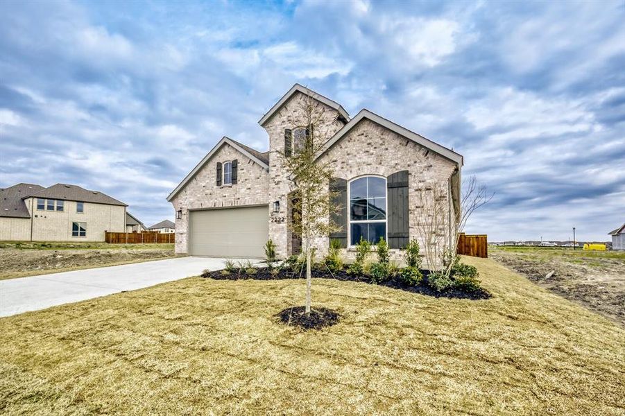 French country inspired facade featuring concrete driveway, brick siding, and a garage