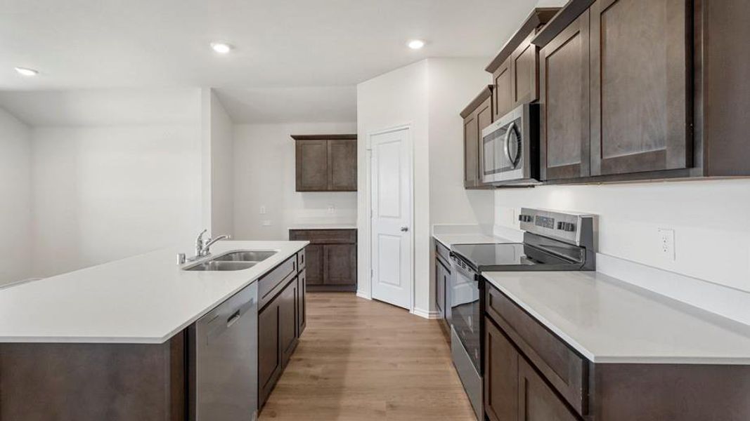 Modern kitchen featuring dark wood-finish cabinetry, light-toned countertops, stainless steel appliances, and wood-finish flooring
