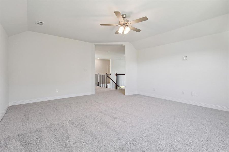 Spare room featuring carpet flooring, ceiling fan, and vaulted ceiling