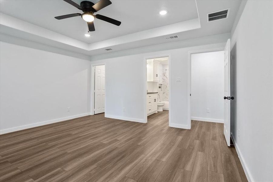 Unfurnished bedroom with a tray ceiling, ensuite bath, hardwood / wood-style flooring, and ceiling fan