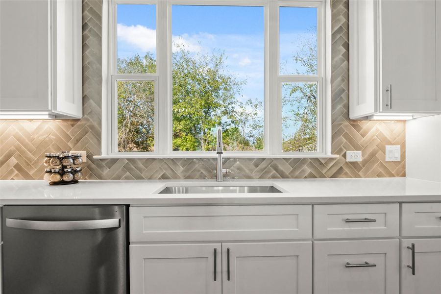Kitchen featuring stainless steel dishwasher, light countertops, white cabinets, and tasteful backsplashThe photos shown are of a completed home with the same floor plan and may not reflect the exact finishes, features, or layout of the home currently under construction. Actual details may vary. Please contact the builder or listing agent for specific information about this property.