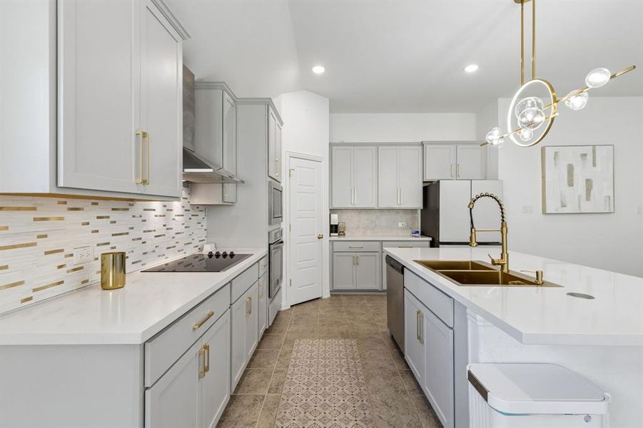 Modern kitchen featuring a large central island with a gold-tone double basin sink and gooseneck faucet