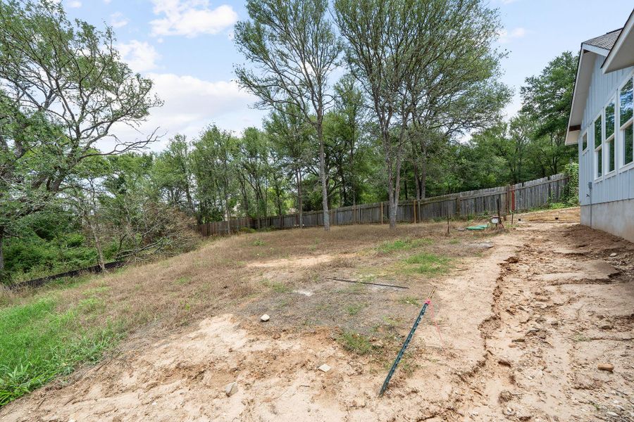 Expansive undeveloped yard with partial fencing and mature trees