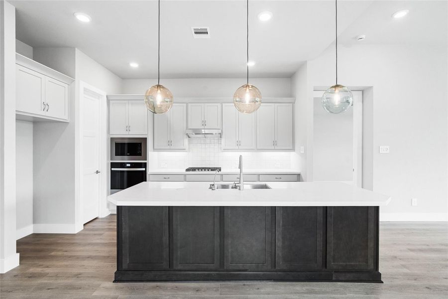 The kitchen anchors the space with light gray perimeter cabinetry, a bold island, a suite of modern stainless steel appliances, and sleek white quartz countertops that create an inviting hub perfect for casual dining or hosting.