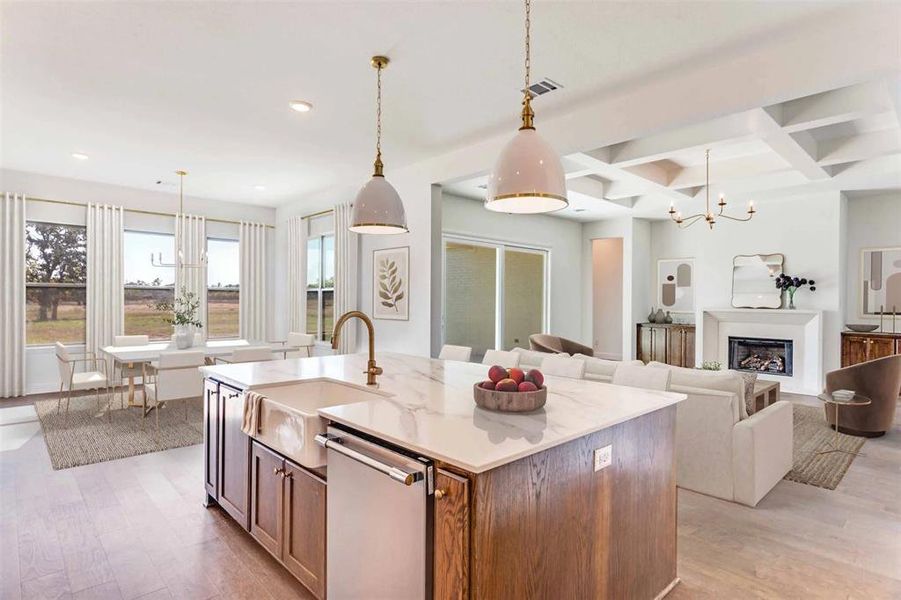 Kitchen featuring a chandelier, pendant lighting, a glass covered fireplace, an island with sink, and light stone counters Kitchen featuring a chandelier, pendant lighting, a glass covered fireplace, an island with sink, and light stone counters