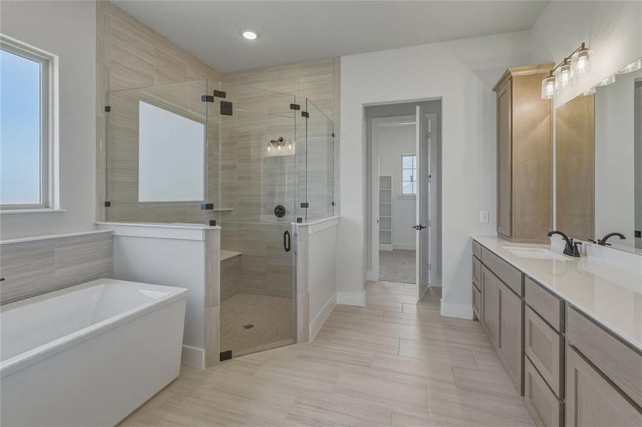 Spacious bathroom featuring a freestanding tub, glass-enclosed shower with a bench, dual vanity, and light wood-finish cabinetry Spacious bathroom featuring a freestanding tub, glass-enclosed shower with a bench, dual vanity, and light wood-finish cabinetry