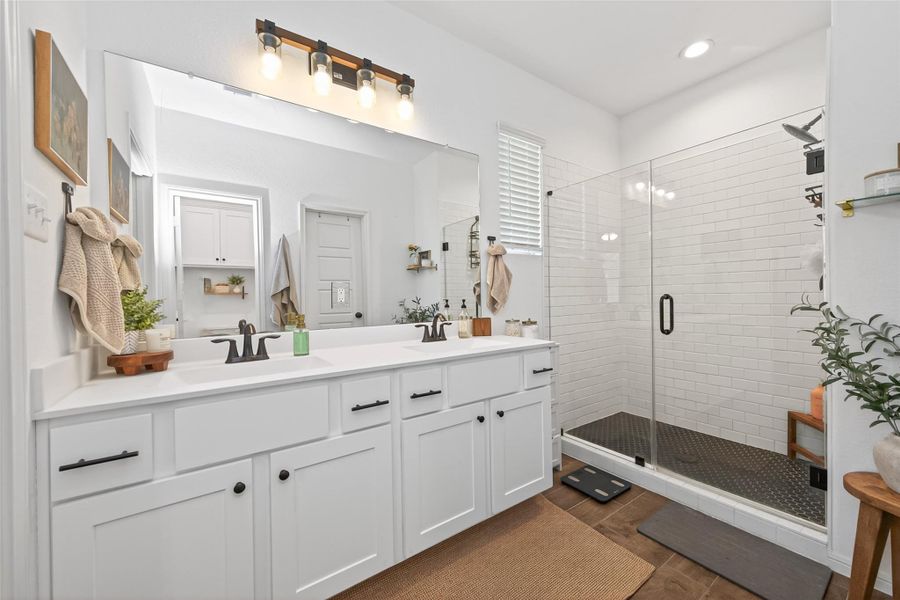 This bathroom features a modern design with a large double sink vanity and stylish bronze fixtures and hardware. It includes a spacious glass frameless shower with white subway tiles, black tiled shower floor complemented by a bright, clean aesthetic and elegant lighting. This bathroom features a modern design with a large double sink vanity and stylish bronze fixtures and hardware. It includes a spacious glass frameless shower with white subway tiles, black tiled shower floor complemented by a bright, clean aesthetic and elegant lighting.