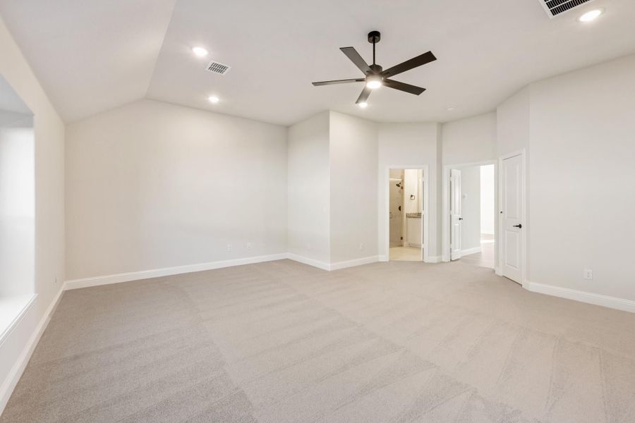 Spacious empty bedroom with beige carpet, ceiling fan, and doorway leading to ensuite bathroom
