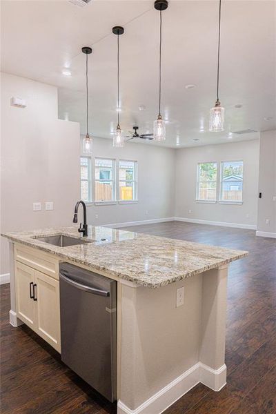 Kitchen with decorative light fixtures, dark wood finished floors, stainless steel dishwasher, light stone countertops, and a center island with sink Kitchen with decorative light fixtures, dark wood finished floors, stainless steel dishwasher, light stone countertops, and a center island with sink