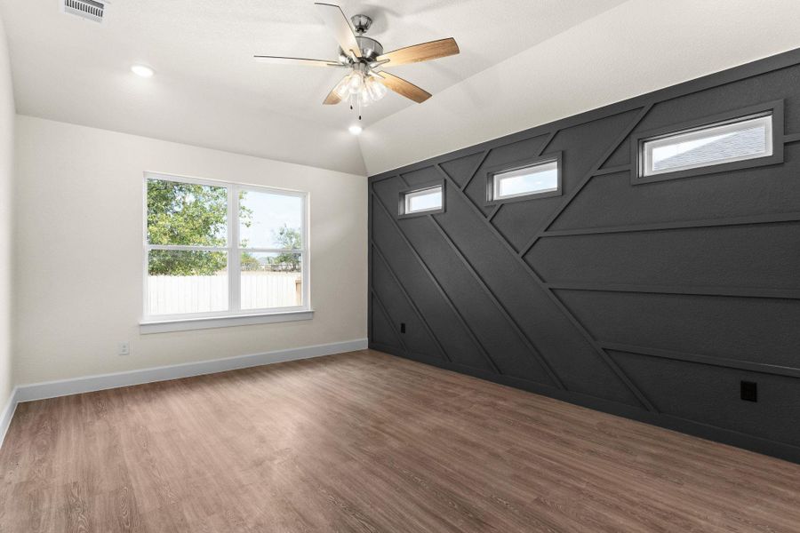 Empty room with wood finished floors, a ceiling fan, vaulted ceiling, recessed lighting, and a decorative wall