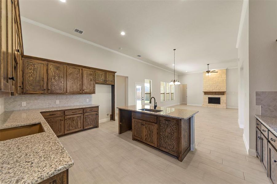 Kitchen with light stone countertops, sink, a fireplace, a center island with sink, and ornamental molding