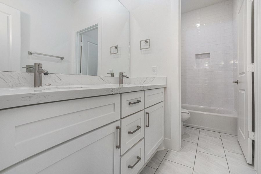 This bathroom features a modern design with a sleek double vanity, marble countertops, and chrome fixtures. It includes a spacious mirror and a tiled shower area with a built-in niche. The bright, neutral tones create a clean and inviting atmosphere. This bathroom features a modern design with a sleek double vanity, marble countertops, and chrome fixtures. It includes a spacious mirror and a tiled shower area with a built-in niche. The bright, neutral tones create a clean and inviting atmosphere.