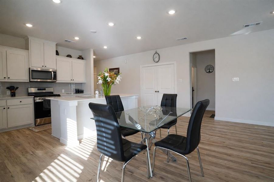 Open-concept kitchen and dining area featuring light-toned wood-finish flooring, recessed lighting, white cabinetry, a kitchen island with seating, and stainless steel appliances