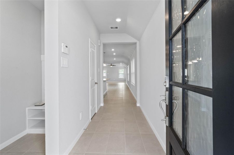 This entryway features a modern, open-concept design. The long, bright corridor utilizes a neutral color palette, recessed lighting, and floor tiles to lead the eye toward the home's main living area.