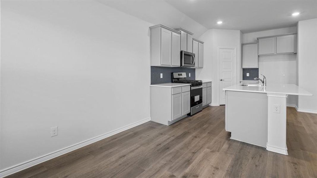 Kitchen featuring appliances with stainless steel finishes, a center island with sink, dark wood-style floors, gray cabinets, and recessed lighting