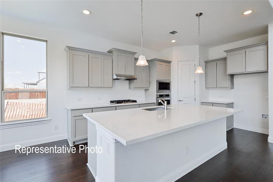 Kitchen with decorative light fixtures, stainless steel appliances, an island with sink, dark wood-type flooring, and gray cabinetry