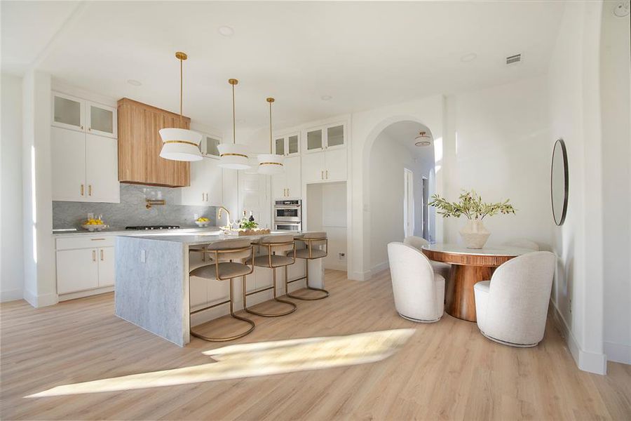 Kitchen featuring a breakfast bar area, glass insert cabinets, white cabinets, arched walkways, and an island with sink Kitchen featuring a breakfast bar area, glass insert cabinets, white cabinets, arched walkways, and an island with sink