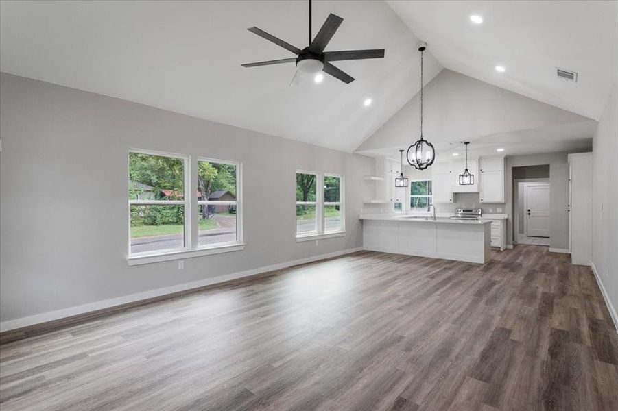 Unfurnished living room featuring hardwood / wood-style floors, ceiling fan with notable chandelier, high vaulted ceiling, and sink