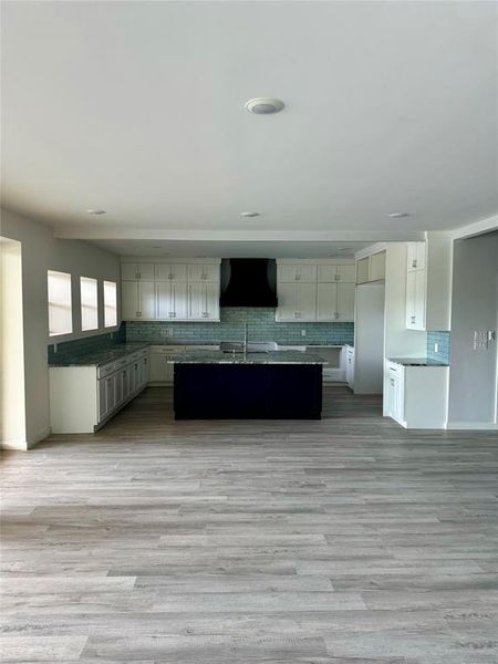 Kitchen featuring decorative backsplash, a center island with sink, light hardwood / wood-style flooring, premium range hood, and sink