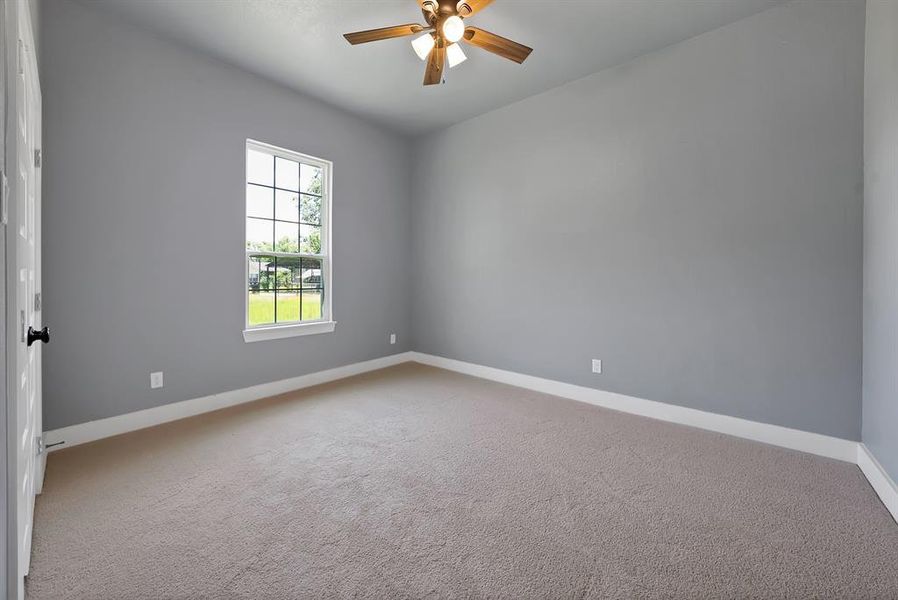 Carpeted room featuring a single window with grid panes, a ceiling fan with light fixture, and neutral gray walls with white baseboards