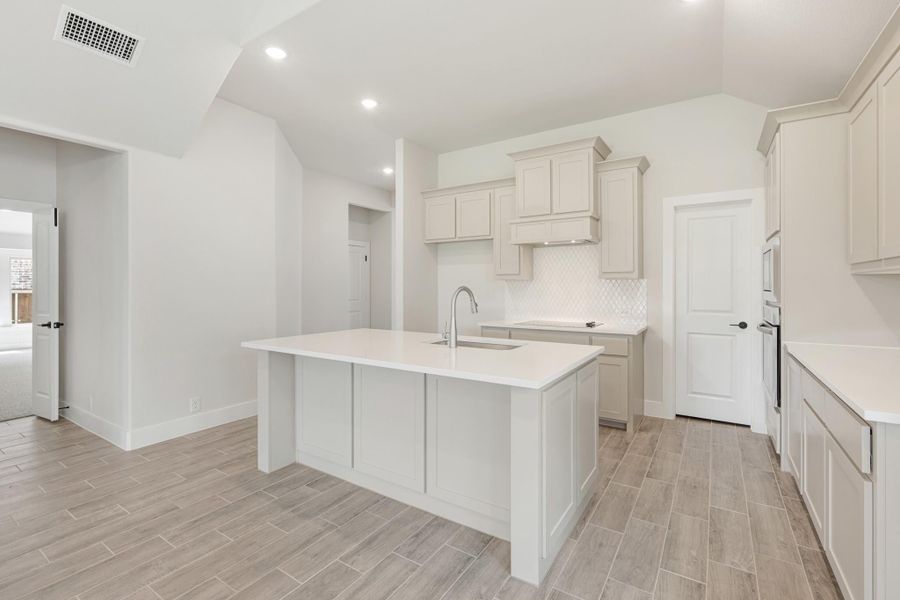 Kitchen with white cabinets, center island with sink, tile backsplash, and wood-look tile floors