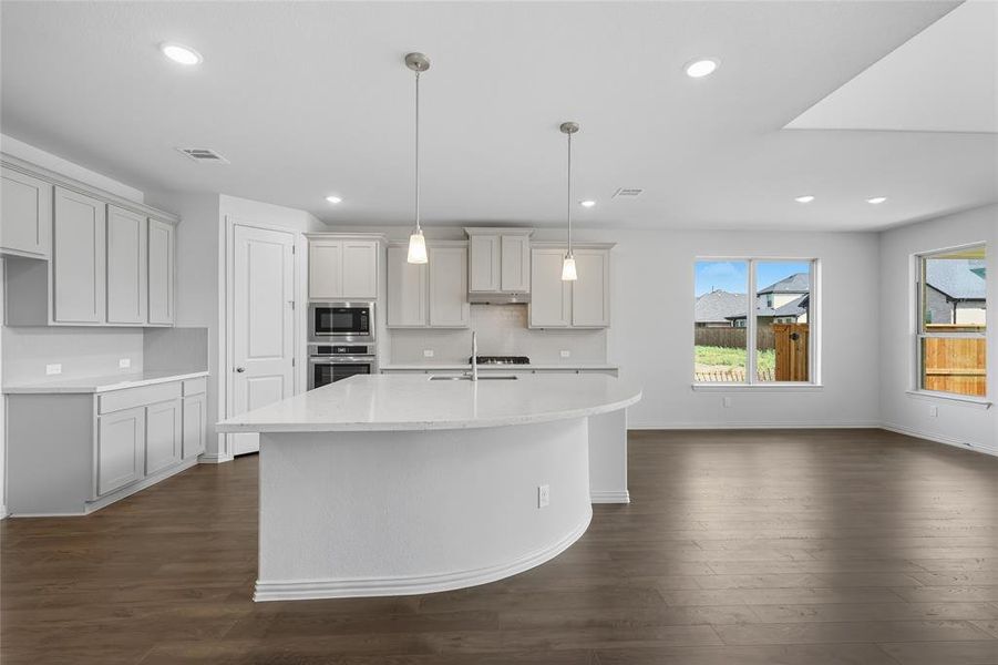 Kitchen featuring a kitchen island with sink, light stone counters, stainless steel appliances, and dark wood finished floors Kitchen featuring a kitchen island with sink, light stone counters, stainless steel appliances, and dark wood finished floors