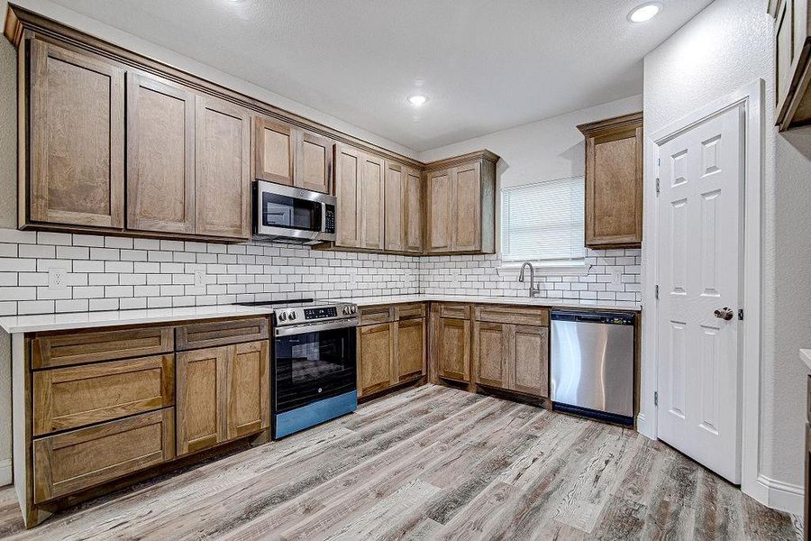 Kitchen with backsplash, sink, stainless steel appliances, and light hardwood / wood-style floors