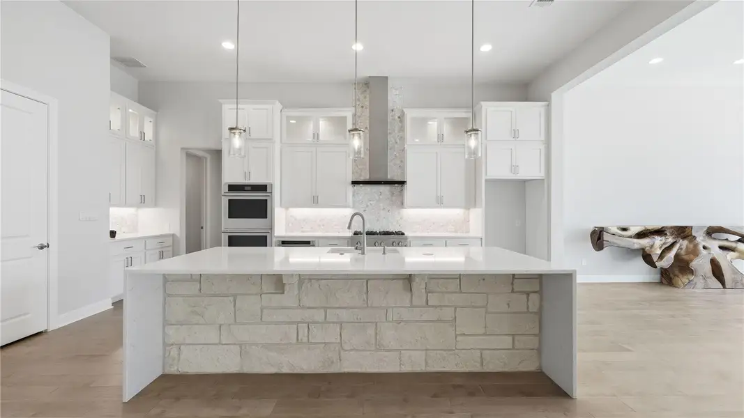 Kitchen with light stone countertops, glass insert cabinets, a breakfast bar area, a large island, and recessed lighting Kitchen with light stone countertops, glass insert cabinets, a breakfast bar area, a large island, and recessed lighting