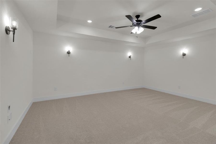 Spacious room featuring neutral carpeting, tray ceiling, recessed lighting, and a ceiling fan