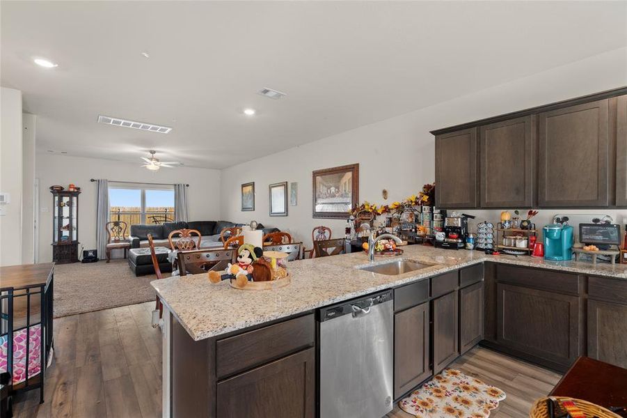 Kitchen featuring dark brown cabinets, light stone counters, stainless steel dishwasher, open floor plan, and dark wood-style flooring