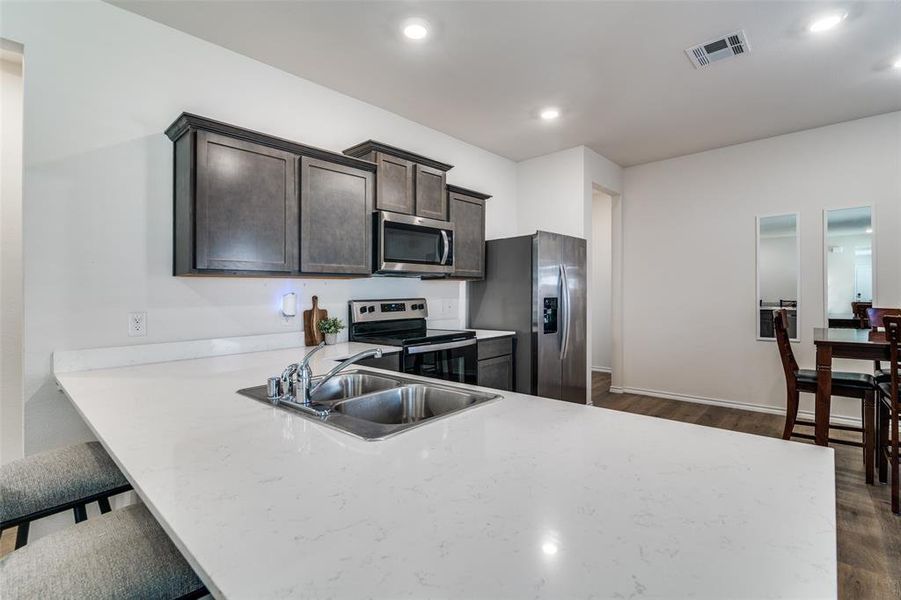 Kitchen with dark wood-style flooring, stainless steel appliances, visible vents, a sink, and dark brown cabinetry