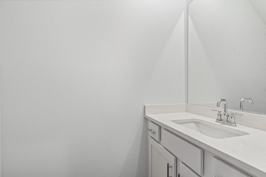 Vanity featuring a white countertop with integrated sink, chrome faucet, and framed mirror