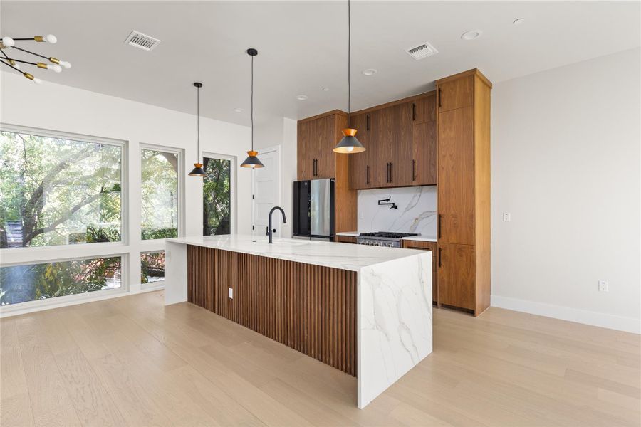 Rich wood cabinetry contrasts beautifully with a marble-veined waterfall island and pale hardwood floors.