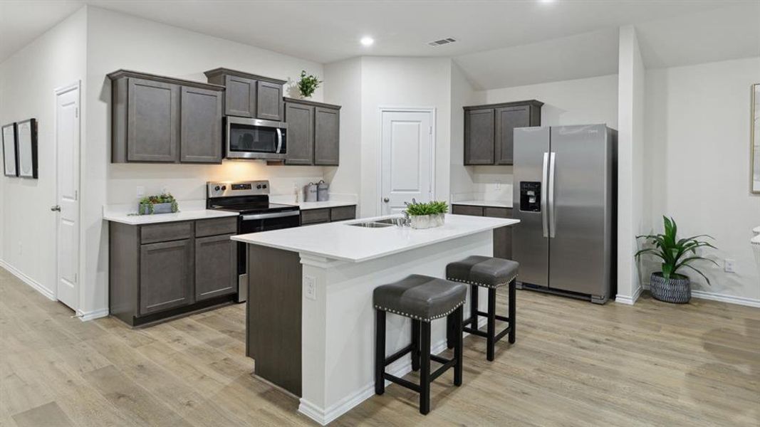 Kitchen with stainless steel appliances, dark wood finish cabinetry, light wood finished floors, a center island with sink, and a breakfast bar area Kitchen with stainless steel appliances, dark wood finish cabinetry, light wood finished floors, a center island with sink, and a breakfast bar area