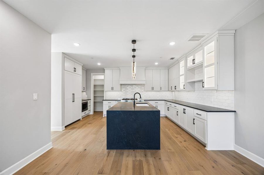 Kitchen with white cabinets, decorative light fixtures, open shelves, and a center island with sink Kitchen with white cabinets, decorative light fixtures, open shelves, and a center island with sink