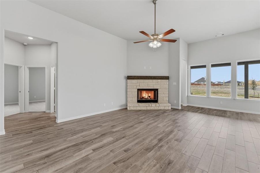 Unfurnished living room with light wood finished floors, a stone fireplace, a high ceiling, ceiling fan, and recessed lighting
