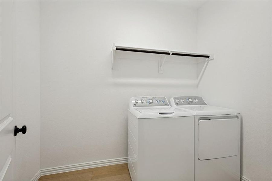 Dedicated laundry space featuring a white washer and dryer, light wood-finish flooring, and a wall-mounted shelf with a hanging rod
