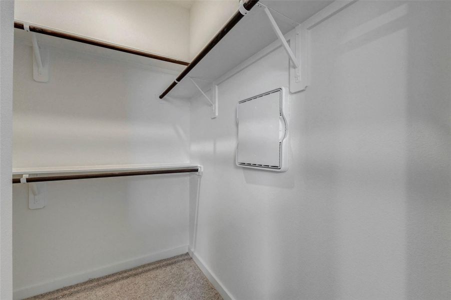 Walk-in closet with built-in shelving and hanging rods, offering practical storage for clothing, shoes, and accessories. The carpeted floor, white walls, and organized layout make this closet a useful extension of the primary suite with room to keep essentials neatly arranged.