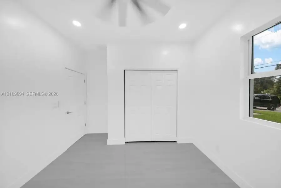 Neutral-toned interior space featuring light grey tile flooring, recessed ceiling lighting, a bi-fold closet, and a single-pane window