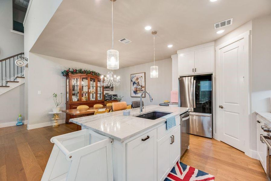 Kitchen with white cabinets, light wood finished floors, stainless steel appliances, an island with sink, and light stone countertops