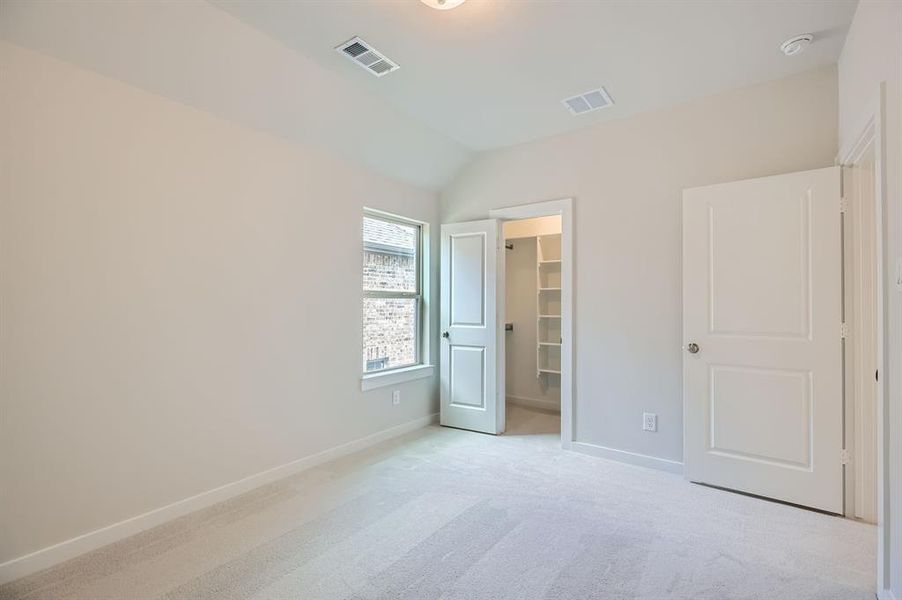 Unfurnished bedroom with a walk in closet, light carpet, and lofted ceiling
