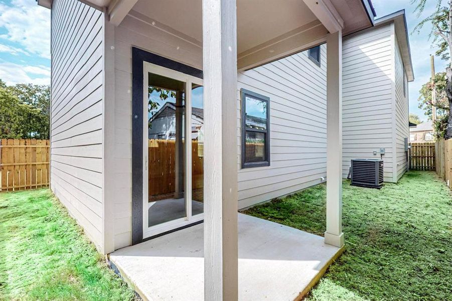 View of exterior entry with central air condition unit, a patio, and a lawn