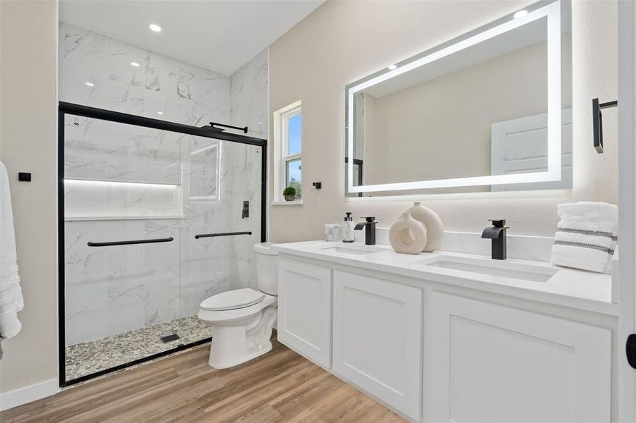 Full bath with a marble finish shower, double vanity, and light wood-style flooring